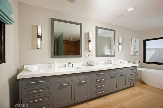 bathroom with a sink, a freestanding tub, wood finished floors, and double vanity