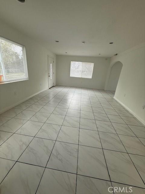 empty room featuring light tile patterned floors, baseboards, and arched walkways