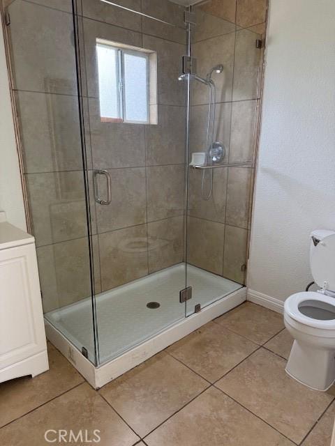 full bath with tile patterned flooring, a stall shower, toilet, and baseboards