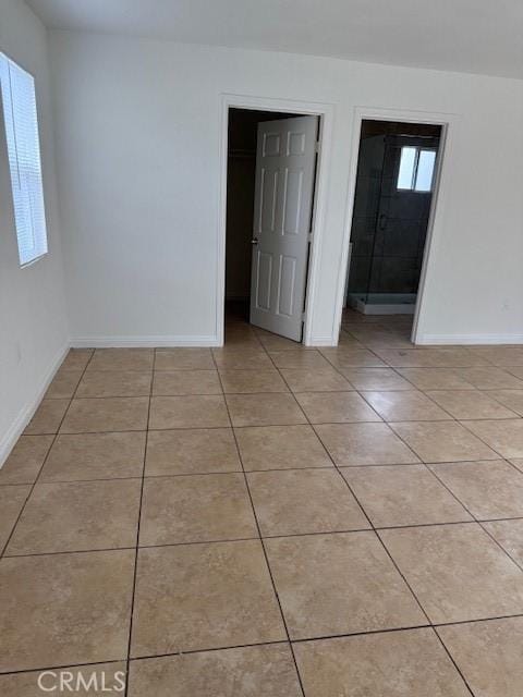 unfurnished bedroom featuring a walk in closet, baseboards, and light tile patterned flooring