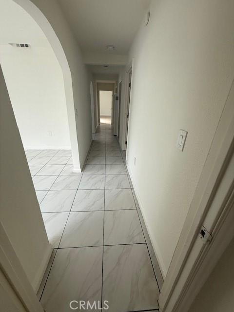 corridor featuring visible vents, arched walkways, marble finish floor, and baseboards