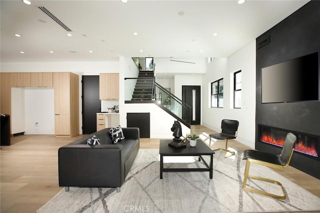 living room featuring light wood-type flooring, stairway, visible vents, and a glass covered fireplace