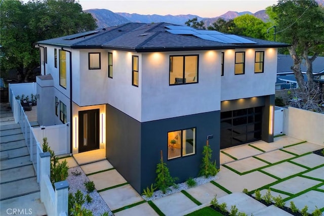 view of front of house with fence, a mountain view, roof mounted solar panels, and stucco siding