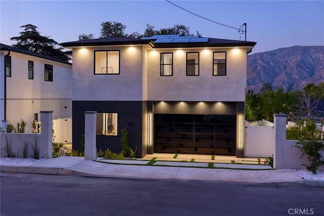 view of front of home with roof mounted solar panels, stucco siding, concrete driveway, and fence