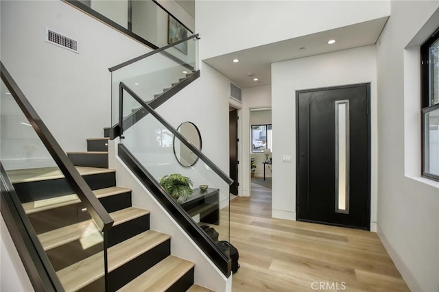 stairway with a high ceiling, wood finished floors, visible vents, and baseboards