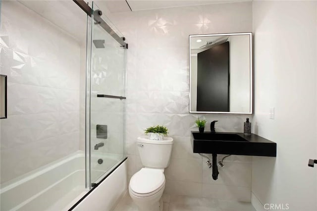 bathroom with tile walls, toilet, and bath / shower combo with glass door