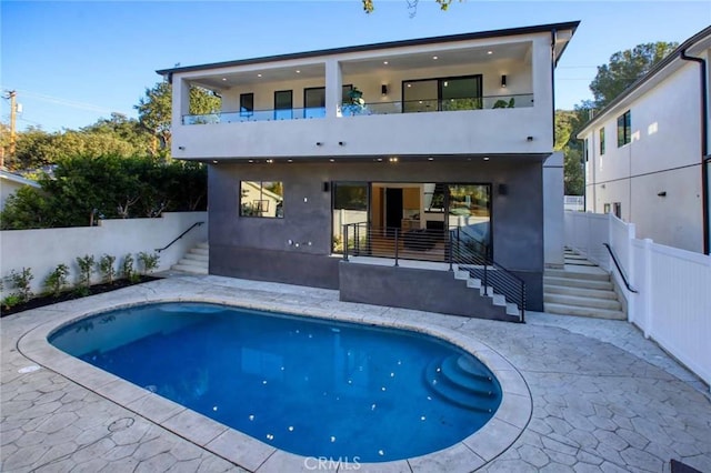 rear view of house with a balcony, a patio area, fence, and stucco siding