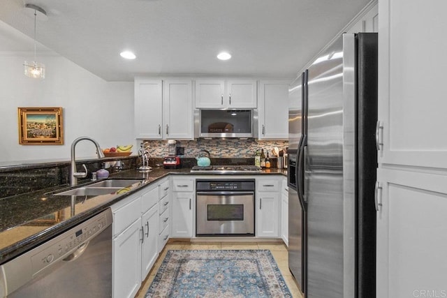 kitchen featuring dark stone counters, decorative backsplash, appliances with stainless steel finishes, white cabinetry, and a sink