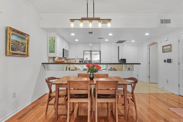 dining room with visible vents, crown molding, baseboards, light wood-type flooring, and arched walkways