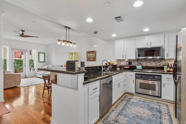 kitchen featuring visible vents, a peninsula, a sink, stainless steel appliances, and open floor plan