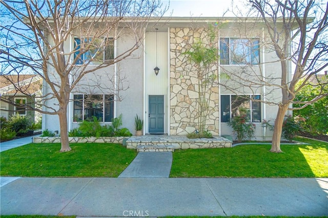 view of front of house featuring stucco siding, stone siding, and a front yard