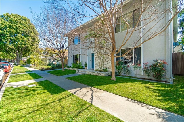 view of front of house with stucco siding, a front lawn, and fence