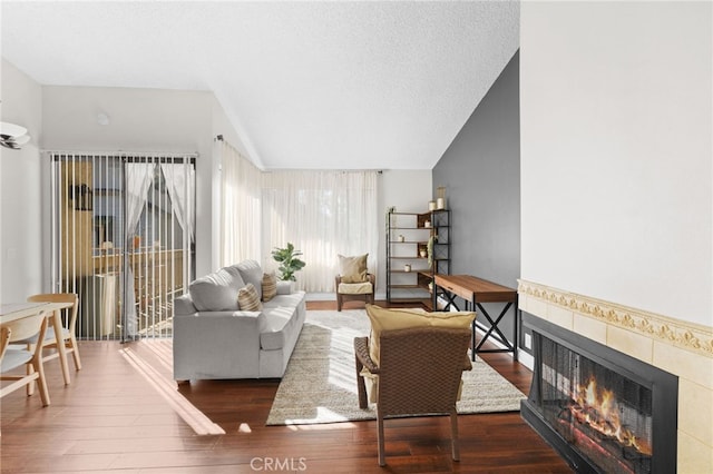 living room with vaulted ceiling, a textured ceiling, a lit fireplace, and wood finished floors