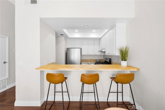 kitchen with under cabinet range hood, appliances with stainless steel finishes, light countertops, and a peninsula