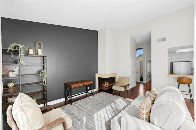 living area with visible vents, baseboards, a lit fireplace, and wood finished floors