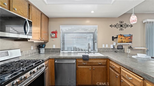 kitchen with a peninsula, a sink, hanging light fixtures, stainless steel appliances, and brown cabinets