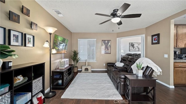 living room featuring visible vents, a textured ceiling, dark wood-style floors, and a ceiling fan