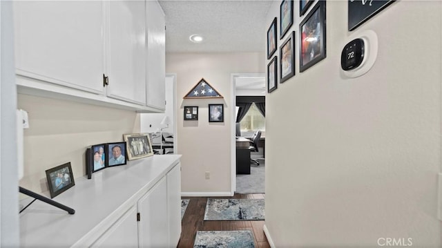 hallway featuring dark wood-style floors, a textured ceiling, and baseboards