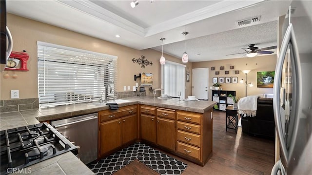 kitchen with visible vents, brown cabinets, a peninsula, stainless steel appliances, and a sink