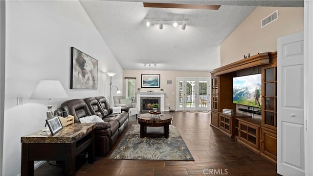 living room featuring visible vents, dark wood-style flooring, a lit fireplace, vaulted ceiling, and a textured ceiling