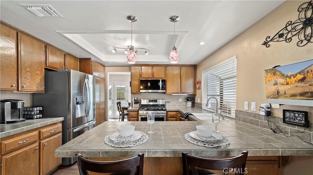 kitchen featuring visible vents, a sink, stainless steel appliances, brown cabinetry, and a raised ceiling