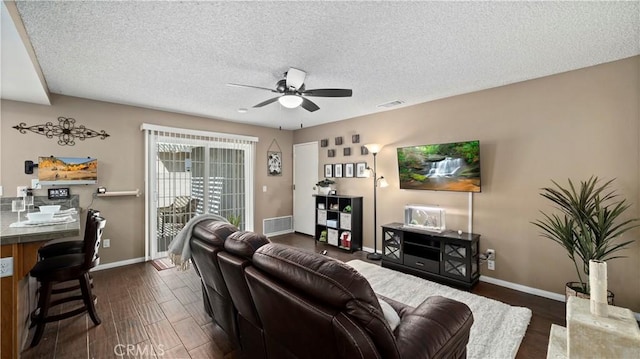 living area with visible vents, dark wood-type flooring, a ceiling fan, a textured ceiling, and baseboards