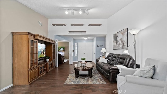 living room with visible vents, a textured ceiling, dark wood-style floors, a high ceiling, and baseboards