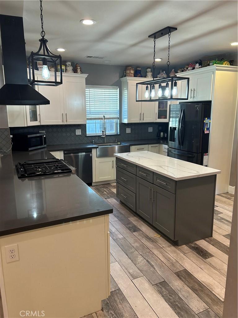 kitchen featuring light wood finished floors, decorative backsplash, island exhaust hood, black appliances, and a sink