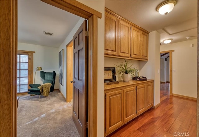 hallway featuring light wood-type flooring, visible vents, baseboards, and light carpet