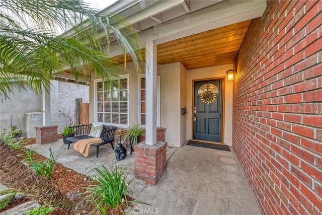 doorway to property with stucco siding, brick siding, and a porch