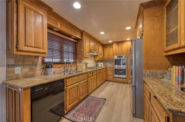 kitchen with under cabinet range hood, light stone counters, light wood-style flooring, stainless steel appliances, and a sink