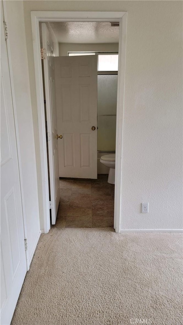 corridor with visible vents, a textured ceiling, carpet floors, baseboards, and a textured wall