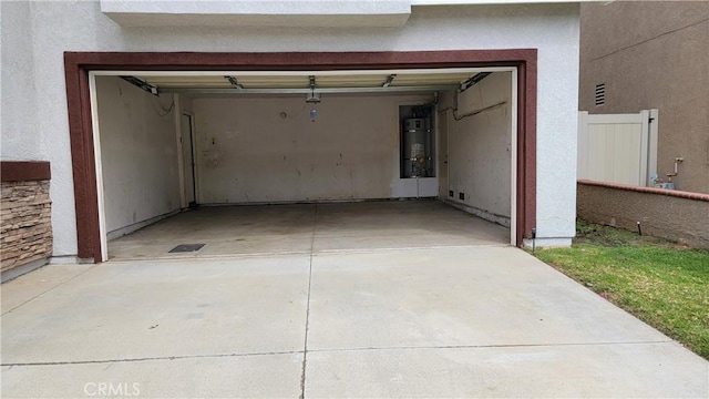 garage with strapped water heater, concrete driveway, and fence