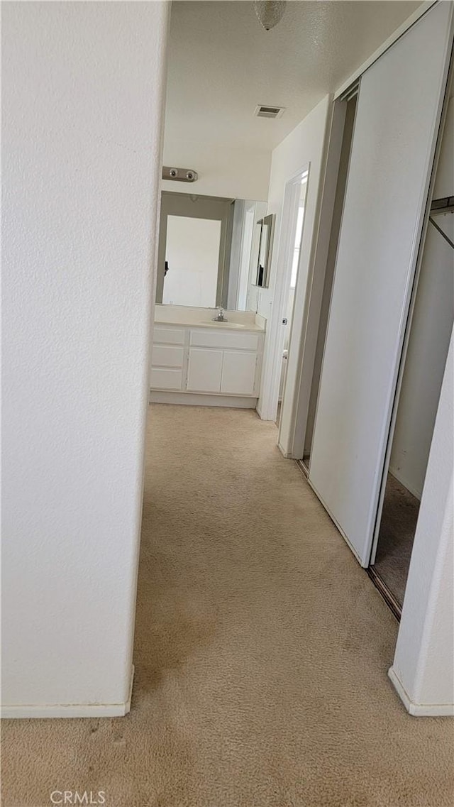 hall with light colored carpet, visible vents, a textured wall, and a sink