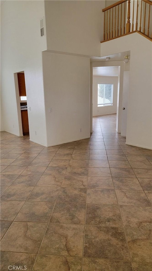 tiled spare room featuring visible vents and a high ceiling