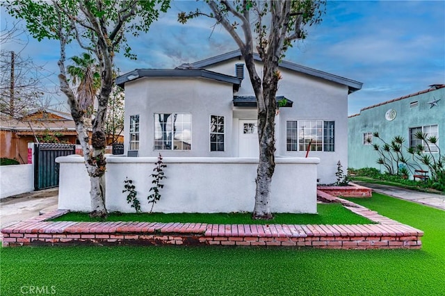 view of front of house featuring stucco siding, a front lawn, and fence