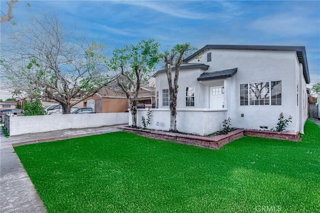 view of front facade with stucco siding, a front yard, and fence