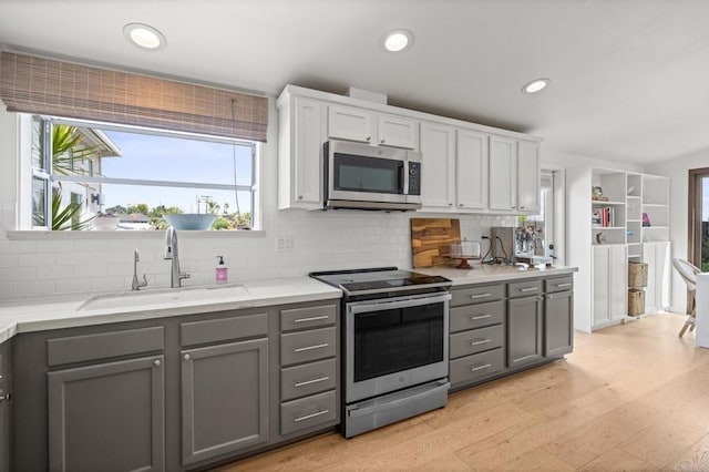 kitchen with a sink, light wood-style flooring, appliances with stainless steel finishes, and gray cabinetry