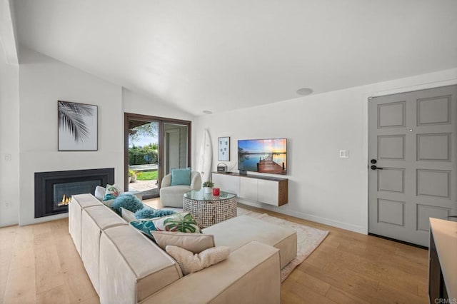 living area featuring vaulted ceiling, light wood-style floors, baseboards, and a warm lit fireplace