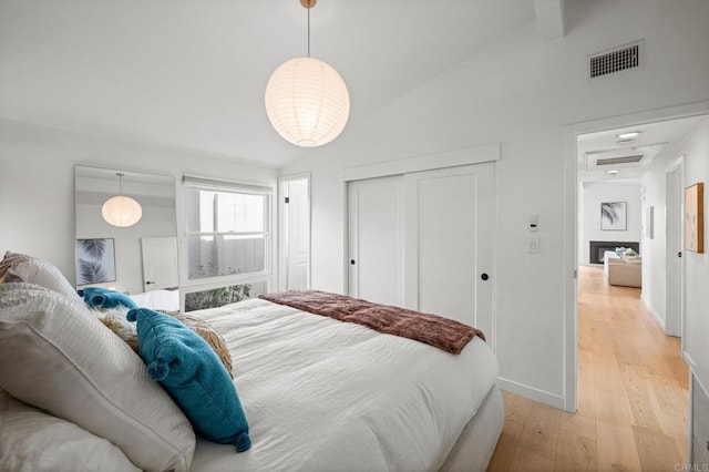 bedroom with baseboards, visible vents, light wood finished floors, lofted ceiling, and a closet