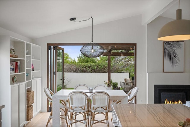 dining space with a warm lit fireplace, light wood-style floors, and vaulted ceiling