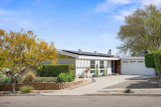 view of front of home with solar panels, an attached garage, a chimney, and driveway