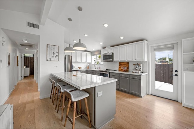 kitchen with visible vents, a breakfast bar area, gray cabinets, stainless steel appliances, and a sink