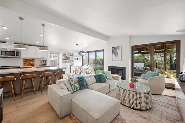 living area featuring a glass covered fireplace, lofted ceiling, light wood-style flooring, and recessed lighting