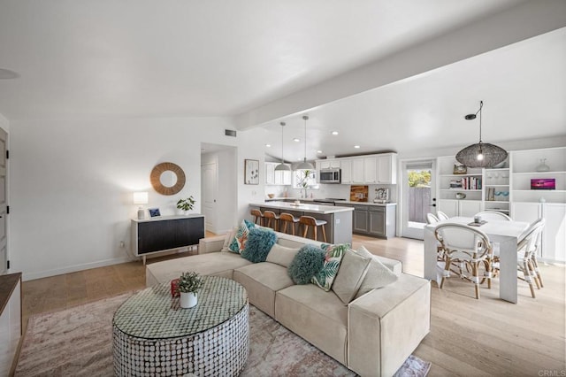 living room featuring visible vents, light wood-type flooring, baseboards, and vaulted ceiling