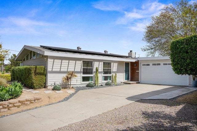 ranch-style home with a chimney, solar panels, an attached garage, and concrete driveway