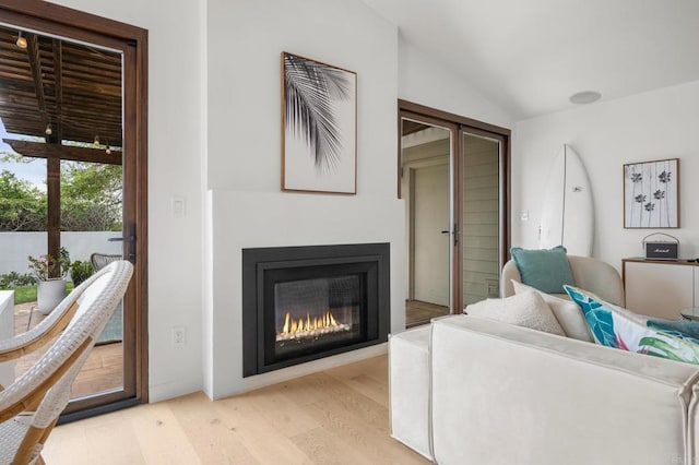 living area with lofted ceiling, a glass covered fireplace, and light wood finished floors