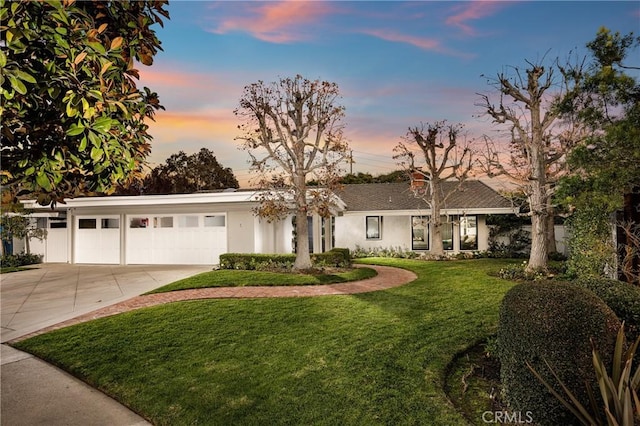 ranch-style home with stucco siding, an attached garage, a lawn, and concrete driveway