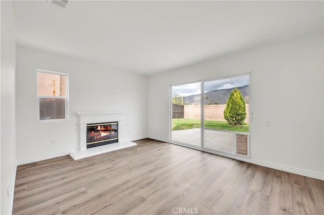 unfurnished living room featuring a glass covered fireplace, baseboards, and wood finished floors