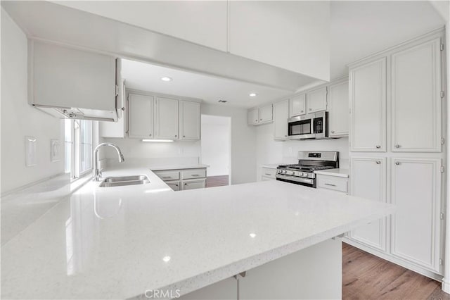 kitchen with light wood-style flooring, a sink, appliances with stainless steel finishes, a peninsula, and light stone countertops